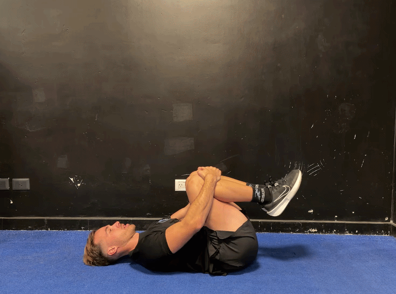 Person demonstrating the knees-to-chest rock exercise